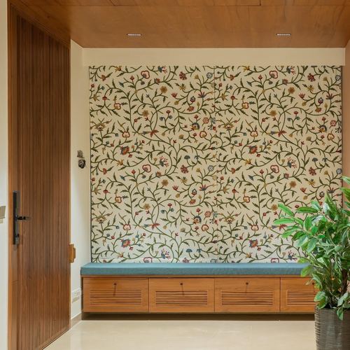 Entryway with floral embroidered wall panel, teal cushioned wooden bench, and potted plant beside a wood-paneled door.