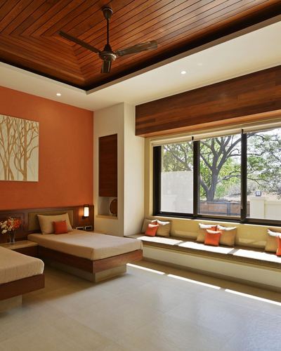 Twin bedroom with orange accent wall, slatted wood ceiling, and sunlit window seat overlooking trees