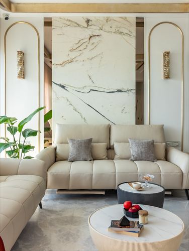 Beige living room with marble accent wall, arched brass niches, tufted sofa and round marble coffee tables