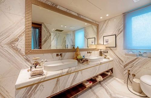 Bathroom with marble-look tile walls, dual oval basins, gold-framed mirror, and brass fixtures