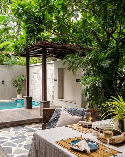 Outdoor dining table with wine glasses beside a plunge pool under a wooden pergola and carved jali wall
