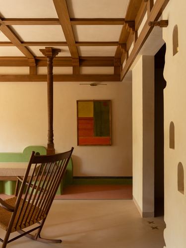 Living room with timber beam ceiling, turned wooden column, rocking chair, and sculpted arched niche wall