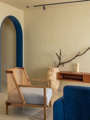 Cane armchair beside blue velvet sofa and arched cobalt niche in plaster-walled living room