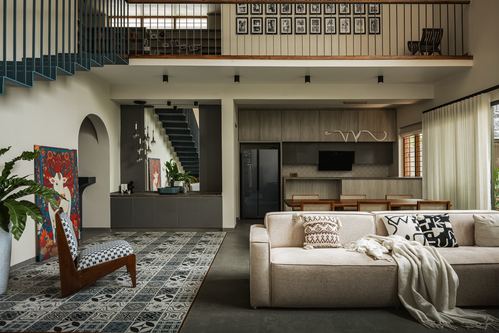 Double-height living room with beige sofa, patterned rug, cane chair, and mezzanine gallery above