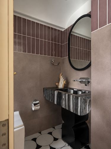 Mauve-tiled bathroom with round black mirror and sculptural veined-stone sink on black pedestal