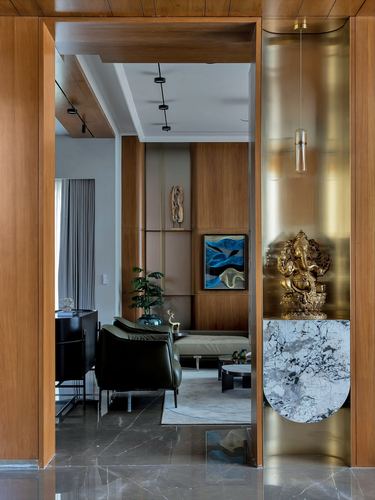 Wooden foyer with brass niche holding a brass Ganesha statue, leading into a warm-toned living room