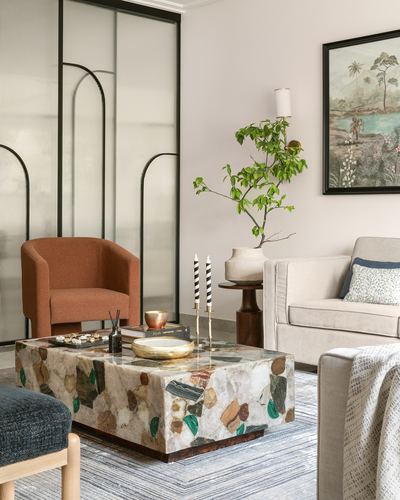 Living room with terrazzo coffee table, rust armchair, reeded glass partition and framed tropical print