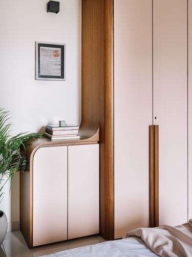 Curved wood-trimmed cabinet with blush doors beside pink wardrobe in bedroom corner