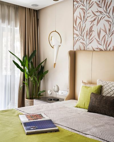 Bedroom corner with beige tufted headboard, leafy wallpaper, plant, and olive green cushions