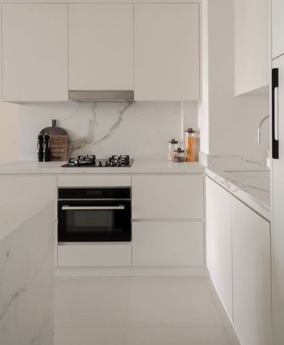 White handle-less kitchen with veined stone backsplash, black gas hob, and integrated oven