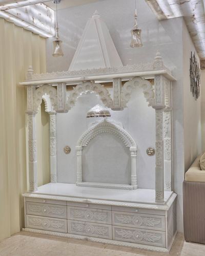 White carved wooden pooja mandir with arched niche and drawer base under pendant lights