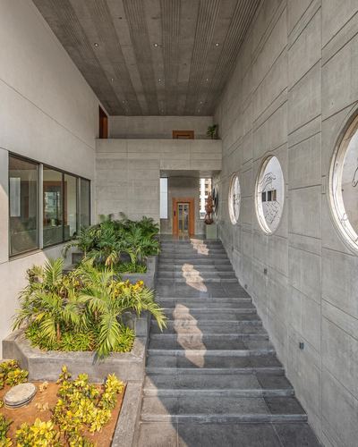 Concrete corridor with steps leading up, porthole windows on right wall, planters on left