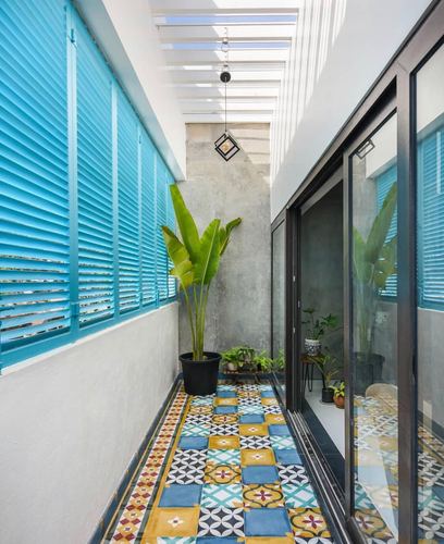Narrow open-to-sky balcony with blue louvered windows, patterned cement tiles and potted plants
