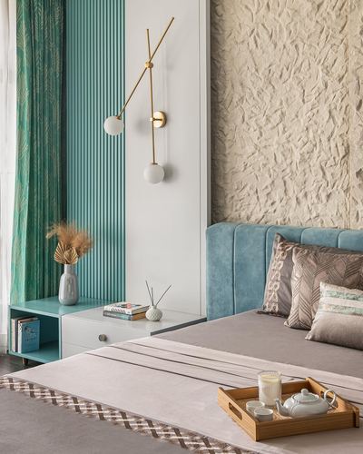 Bedroom corner with teal fluted panel, brass sconce, textured stone wall, and blue velvet headboard with tray of tea set