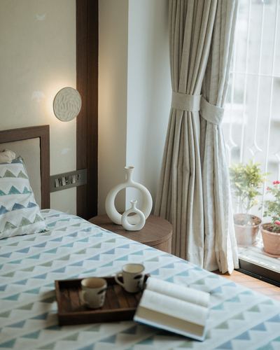 Bedside vignette with white ceramic vases, linen curtains and patterned bedding in soft daylight