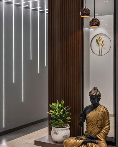 Buddha statue and potted plant beside fluted wood panel with linear ceiling lighting