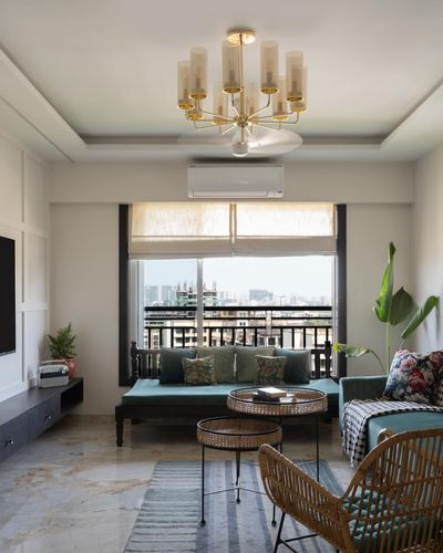Living room with teal daybed under a black-framed window, brass chandelier above, city view beyond