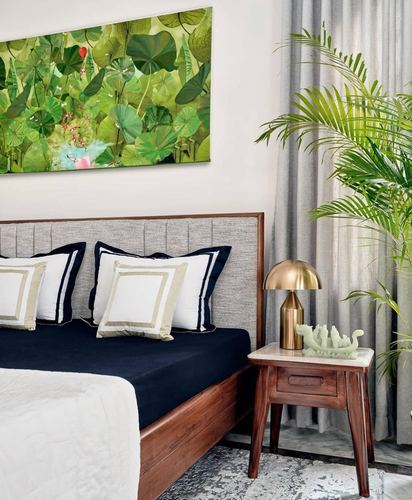 Bedroom corner with tufted grey headboard, navy bedding, wooden nightstand, brass lamp and large potted palm