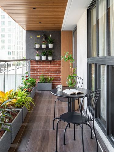 Narrow balcony with wood ceiling, brick wall, potted plants, and black bistro table with chairs