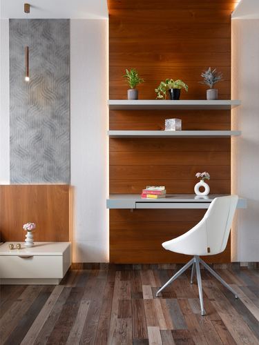 Built-in wood-veneer study nook with floating shelves, desk, and white swivel chair on wood floor