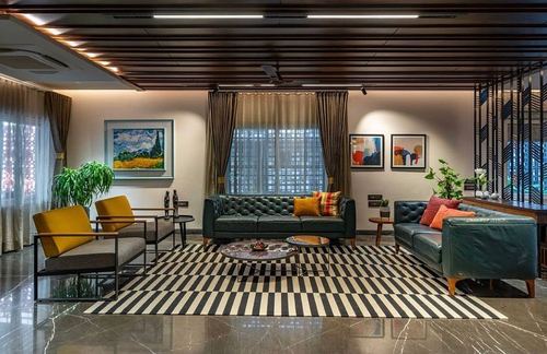 Living room with green tufted sofas, mustard chairs, striped rug and slatted wood ceiling