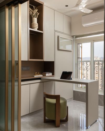 Built-in study nook with beige cabinetry, brass-lined sliding door, and green upholstered chair beside window