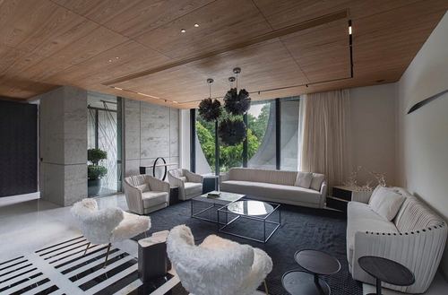 Modern living room with wood-clad ceiling, concrete wall panels, black rug and white sofas facing glass facade