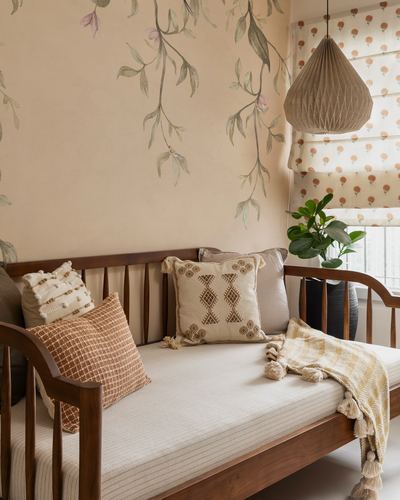 Wooden daybed with patterned cushions beneath a hand-painted leafy mural and woven pendant light