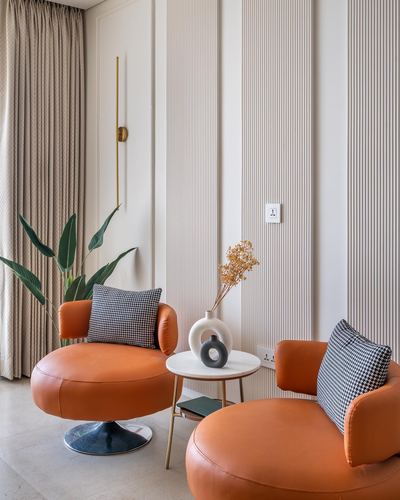 Two orange round swivel chairs with houndstooth cushions beside a marble side table on fluted wall