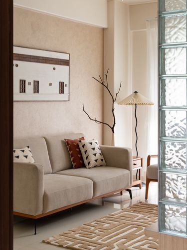 Beige living room corner with sofa, patterned cushions, pleated lamp and glass block wall