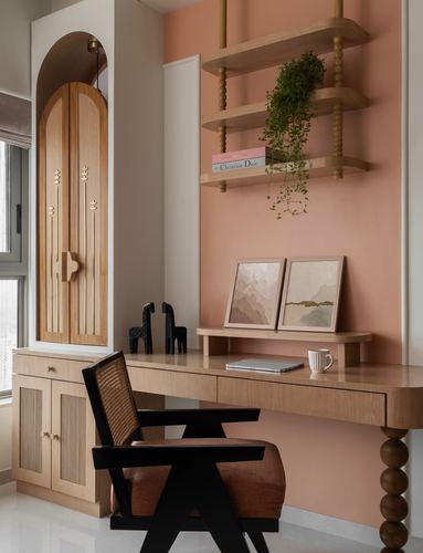 Pink-walled study nook with arched wooden wardrobe, floating desk, cane chair, and hanging plant shelf