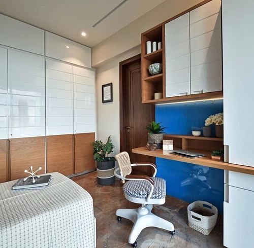 Study nook with wooden desk, cane-back chair, and blue glass backsplash beside white wardrobes