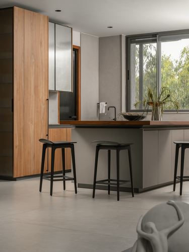 Contemporary kitchen island with black stools, wood cabinetry, and a glass wall view of trees