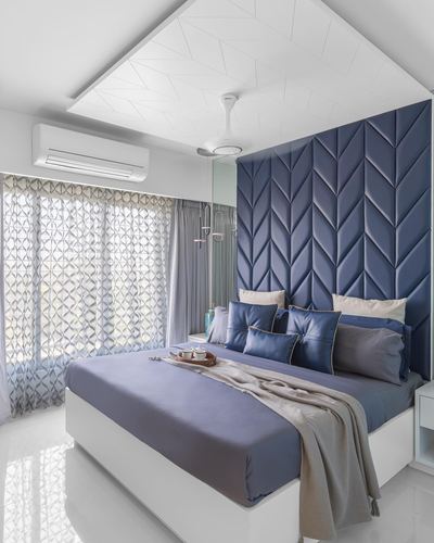 Bedroom with tall navy chevron-tufted headboard wall, patterned white ceiling, and sheer curtained window