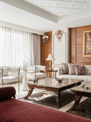 Formal living room with marble coffee tables, cream tufted sofas, maroon velvet seating, wood-paneled wall