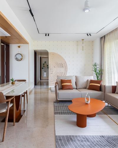 Living room with beige sofa, orange coffee table and carved circular jali partition on patterned wall