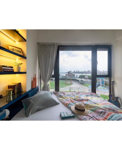 Bedroom with backlit blue shelving, striped bedspread, guitar, and window overlooking sea view