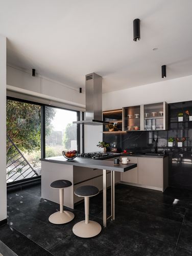 Modern black-and-taupe kitchen with island, stainless hood, and large view window to greenery