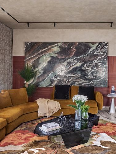 Mustard velvet sectional sofa facing a dark swirling stone panel above wood paneling