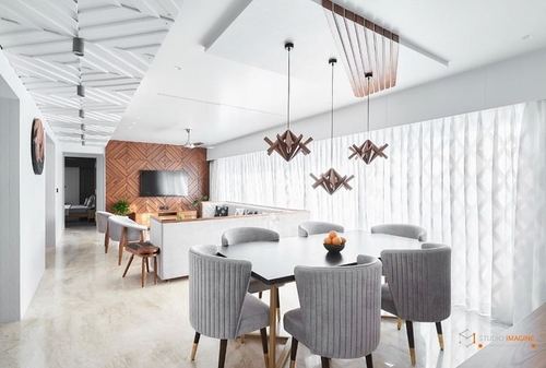 Open dining and living area with black table, grey velvet chairs, and sculptural wood pendants