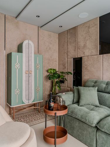 Living room corner with green art deco cabinet, sage sofa, and leather bar cart against padded beige wall