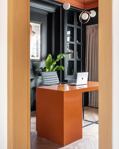 View through a doorway into a home office with an orange desk and black shelving