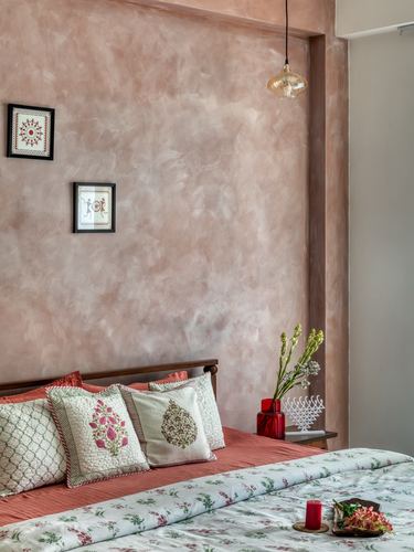 Bedroom with textured pink plaster wall, block-print bedding, and warli art frames in Pune home