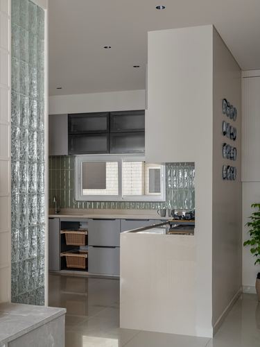 Kitchen seen past a glass block column, with sage tile backsplash, grey cabinetry and wicker storage baskets