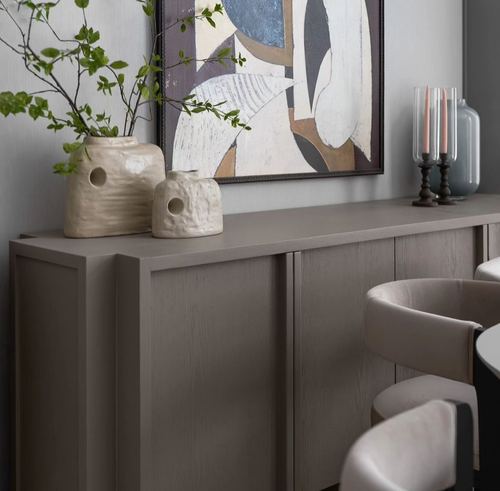 Griege wood sideboard with textured ceramic vases beneath abstract artwork in a dining area