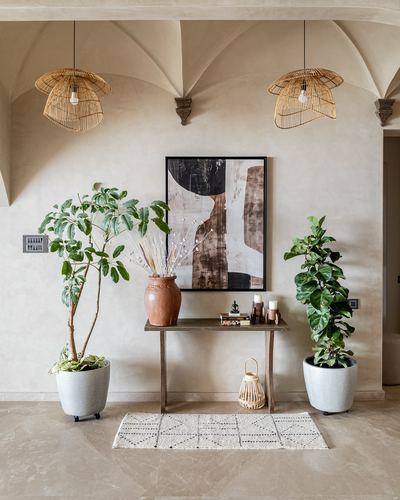 Foyer with vaulted plaster ceiling, rattan pendants, wooden console, abstract art, and two potted plants