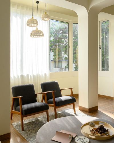 Two mid-century armchairs beneath cane pendant lights under an arched cutout wall by a sunlit window