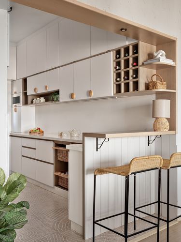 White kitchen with wood-trimmed opening, wine rack, and rattan bar stools at counter