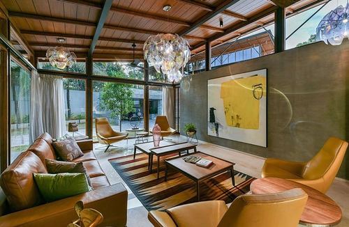 Living room with tan leather sofas, timber ceiling trusses, glass walls, and a yellow abstract painting