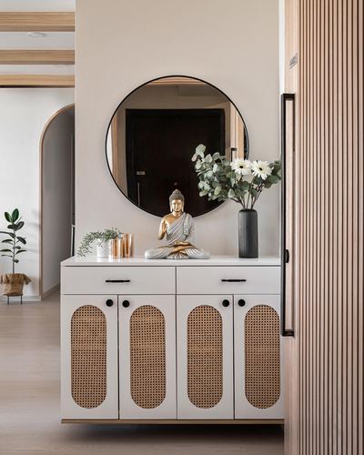 White cane-front console with buddha statue, round mirror and fluted wood panelling in foyer